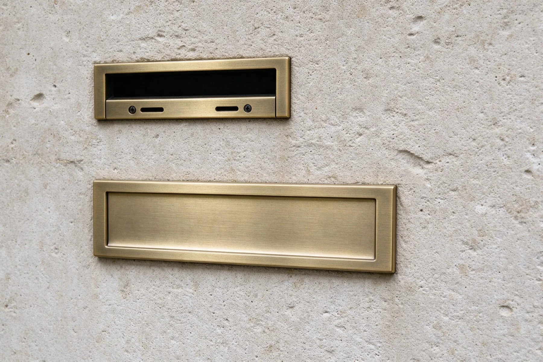 Dezentes Klingelschild aus gebürstetem Metall an einer hellen Sandsteinwand.