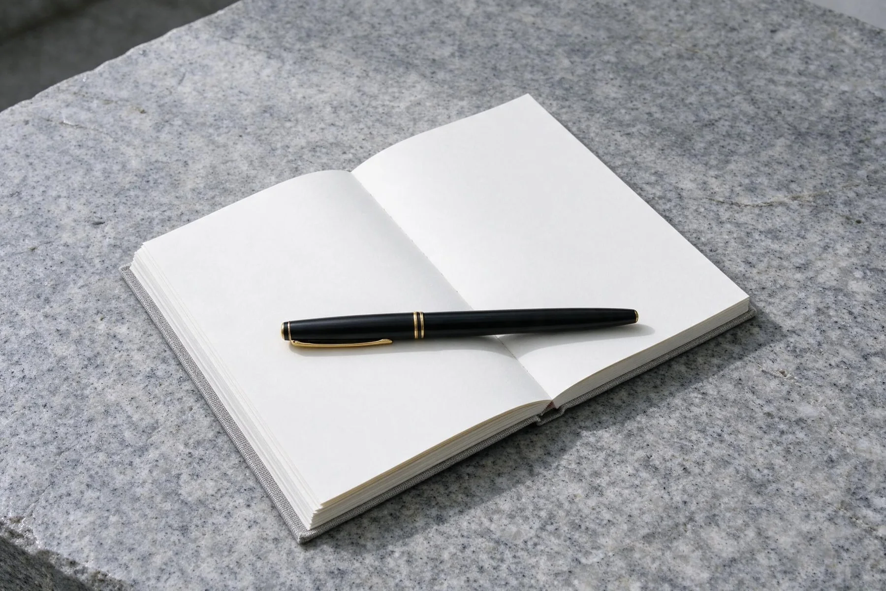 Füllfederhalter auf glattem Granitstein neben einem Notizbuch.